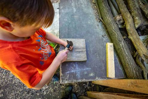 Kind schlägt einen Nagel mit einem Hammer in Holz